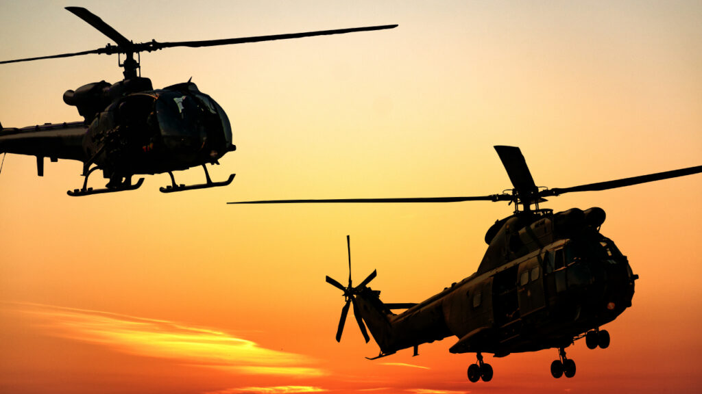 Two helicopters silhouetted against a vibrant orange sunset sky, conveying a sense of motion and adventure.